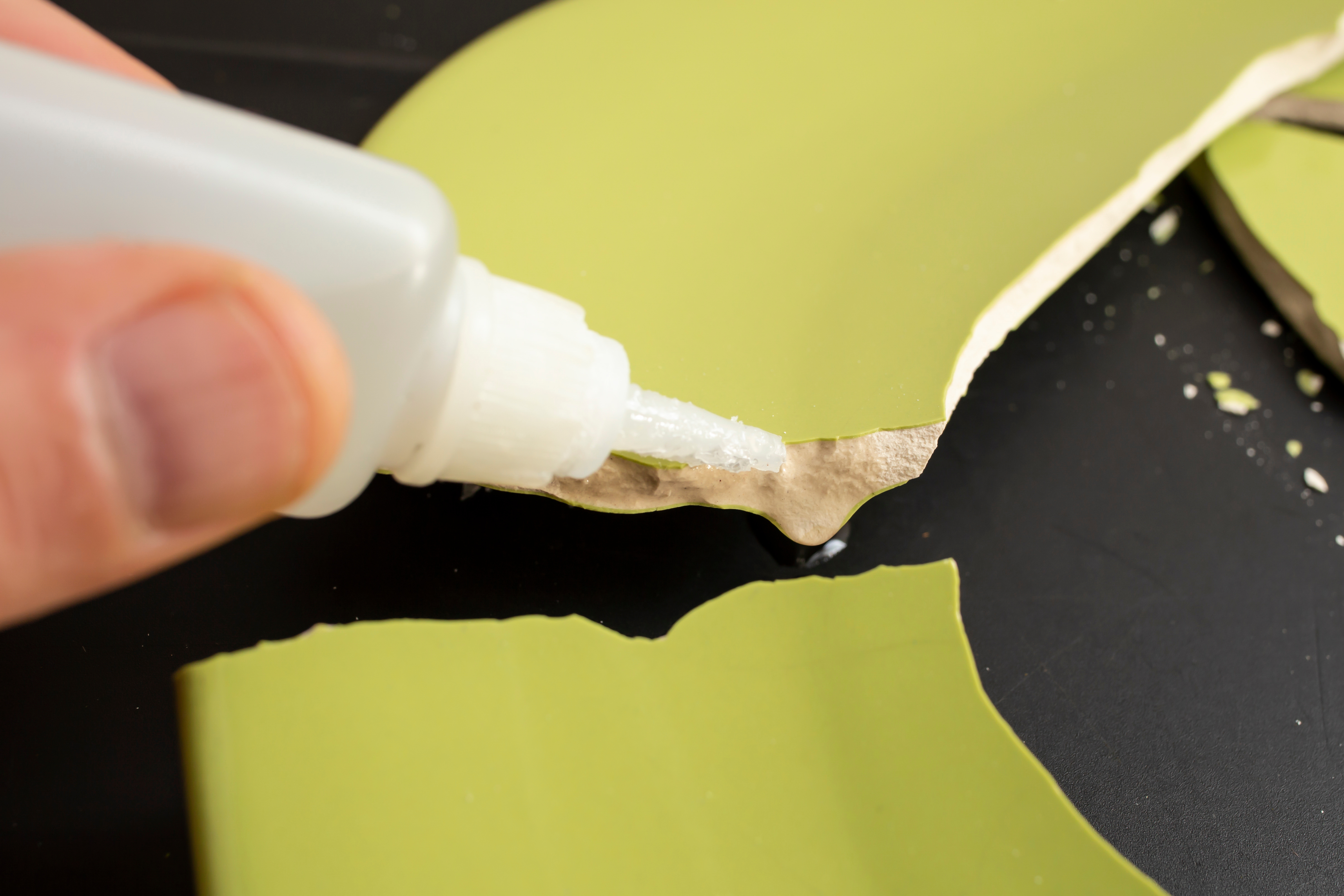 Hand applying liquid glue on ceramic broken pieces, repairing a